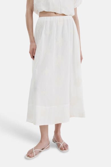 Jupe longue beige de MANGO avec des motifs floraux brodés, portée avec des sandales à brides.
