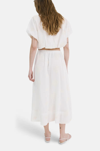 Jupe longue beige de MANGO, à motif discret, portée avec un haut court blanc et des sandales plates.
