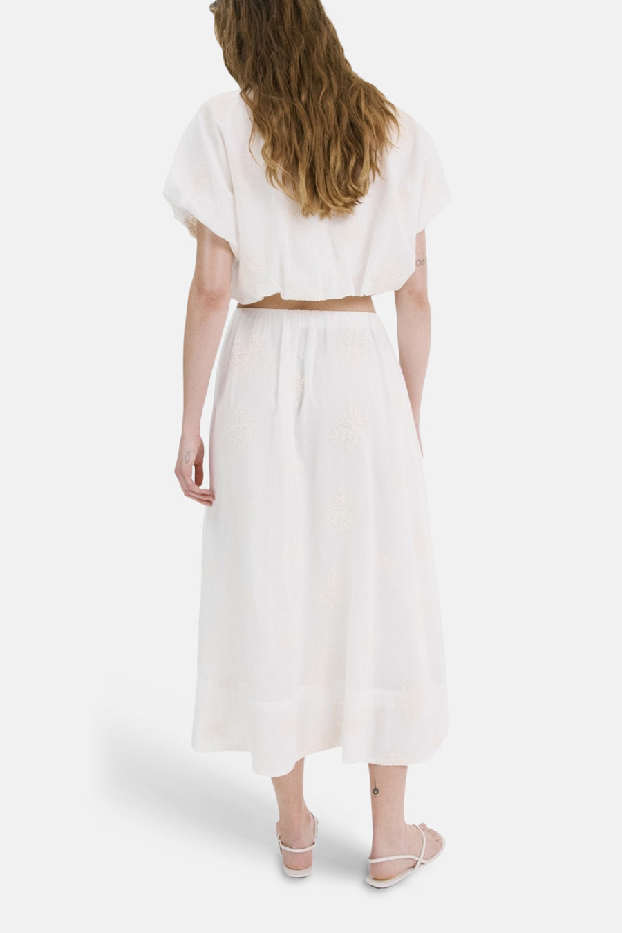 Jupe longue beige de MANGO, à motif discret, portée avec un haut court blanc et des sandales plates.