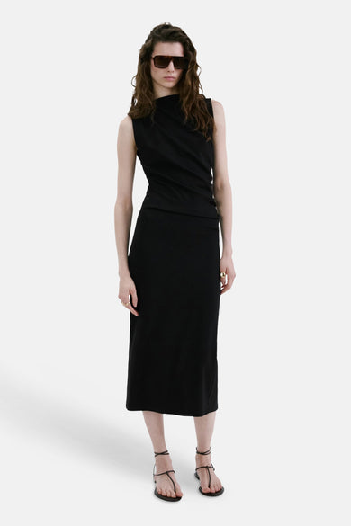 Robe noire de MANGO, sans manches, col montant, longueur midi, portée avec des lunettes de soleil et des sandales.