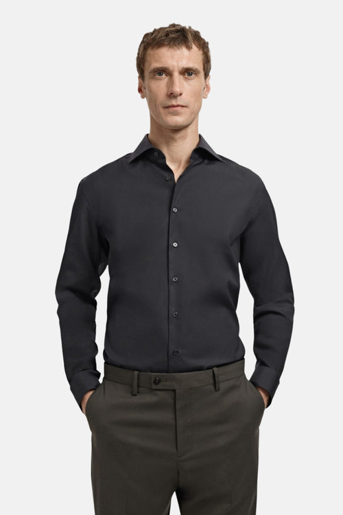 Chemise noire à manches longues de MANGO, portée avec un pantalon vert olive.