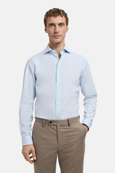 Blauw overhemd met lange mouwen van MANGO, gedragen met een bruin pak, op een witte achtergrond.