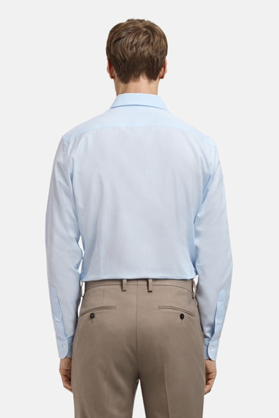 Chemise à manches longues bleue de MANGO, vue de dos, portée avec un pantalon beige.