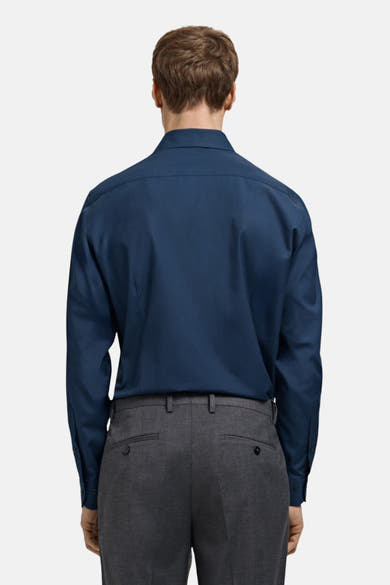 Chemise à manches longues bleue de MANGO, vue de dos, portée avec un pantalon de costume gris.