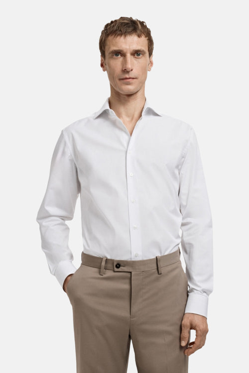 Chemise blanche à manches longues de MANGO, portée avec un pantalon beige uni.