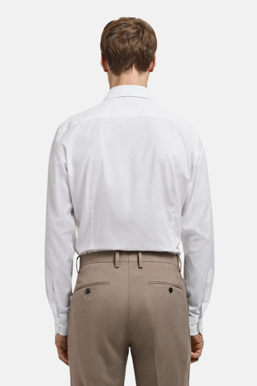 Chemise à manches longues blanche de MANGO, vue de dos, portée avec un pantalon beige.