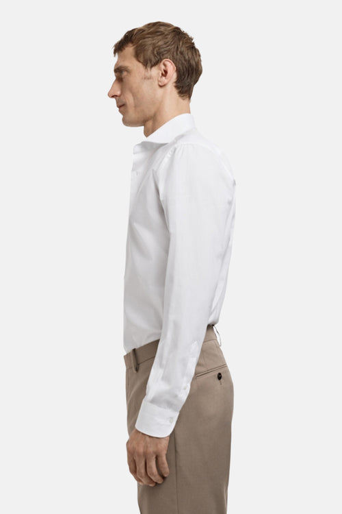 Chemise blanche à manches longues de MANGO, portée avec un pantalon couleur sable, vue de profil.
