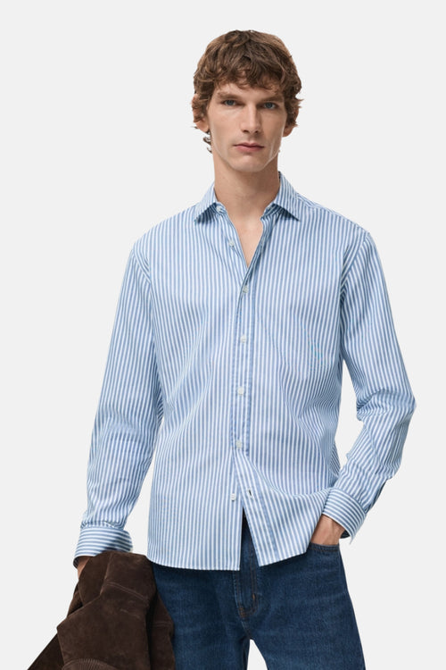 Chemise bleue rayée à manches longues de MANGO, portée avec un jean et une veste en daim.

