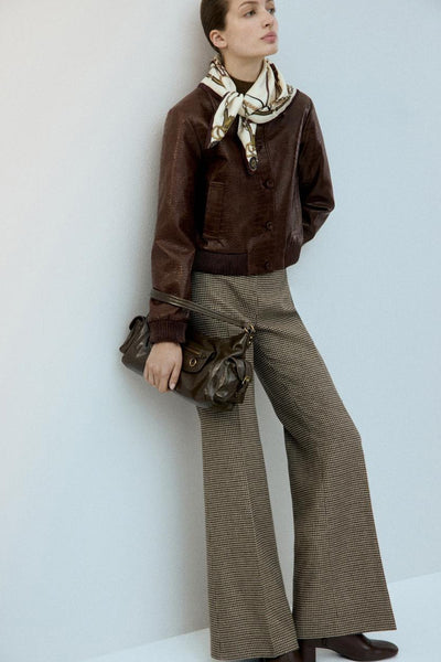 Veste courte brun en cuir, par MANGO, avec un foulard à motifs, un pantalon à carreaux et un sac à main.