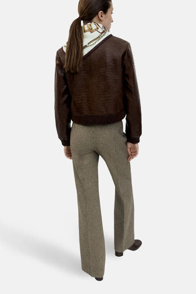 Veste courte brun de MANGO en similicuir à motif crocodile portée avec pantalon à carreaux.