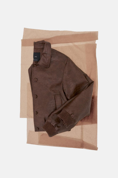 Kort bruin leren jasje van MANGO, op een achtergrond van beige tissuepapier.