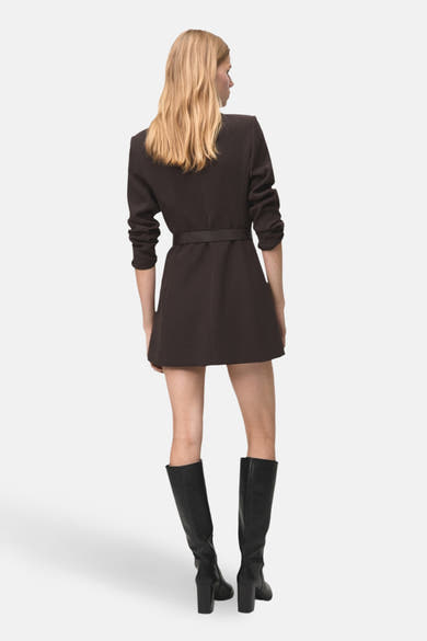Robe à manches longues marron de MANGO, avec une ceinture, portée avec des bottes noires à talons. Vue de dos.