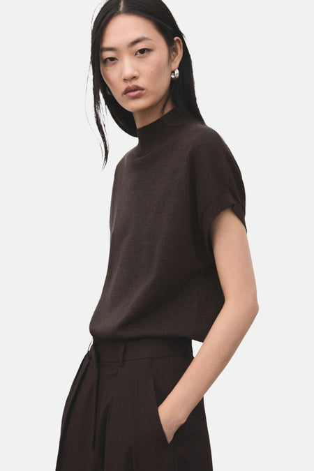 Pull à col rond brun de MANGO, porté avec un pantalon marron à plis et des boucles d'oreilles argentées.