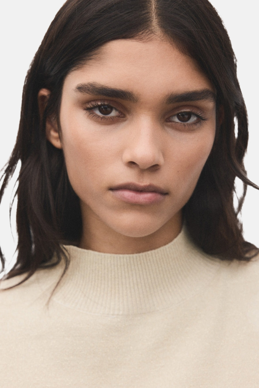 Gouden trui met ronde hals van MANGO, gedragen met los bruin haar en neutrale make-up.