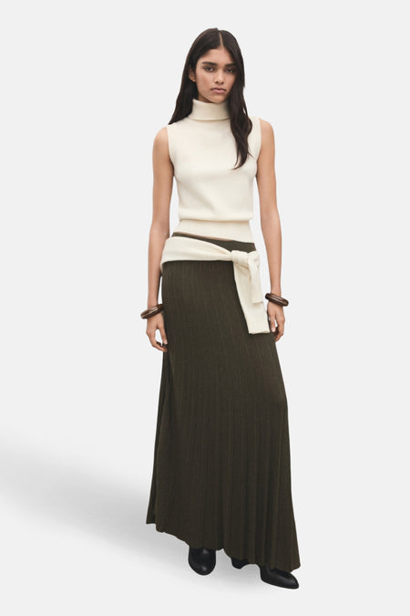 Débardeur écru de MANGO, col roulé sans manches, porté avec une longue jupe vert foncé et une ceinture en tissu nouée.