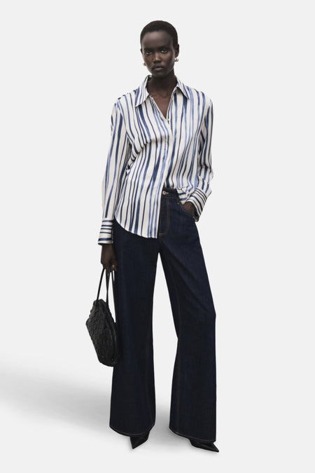 Chemisier multicolore à manches longues de MANGO, à rayures bleues et blanches, porté avec un jean et un sac noir.
