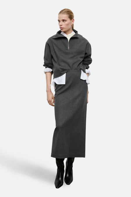 Jupe longue grise de MANGO, coupe droite, portée avec un pull gris zippé et des bottines noires.
