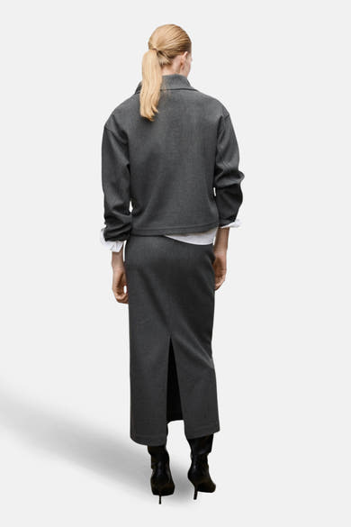 Jupe longue grise de MANGO, avec une fente à l'arrière, portée avec un blazer et des bottes noires.