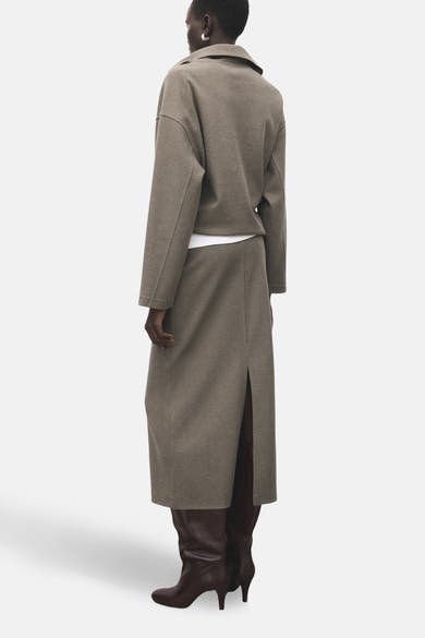 Jupe longue marron de MANGO, fendue à l'arrière, portée avec un haut court blanc et des bottes en cuir marron.