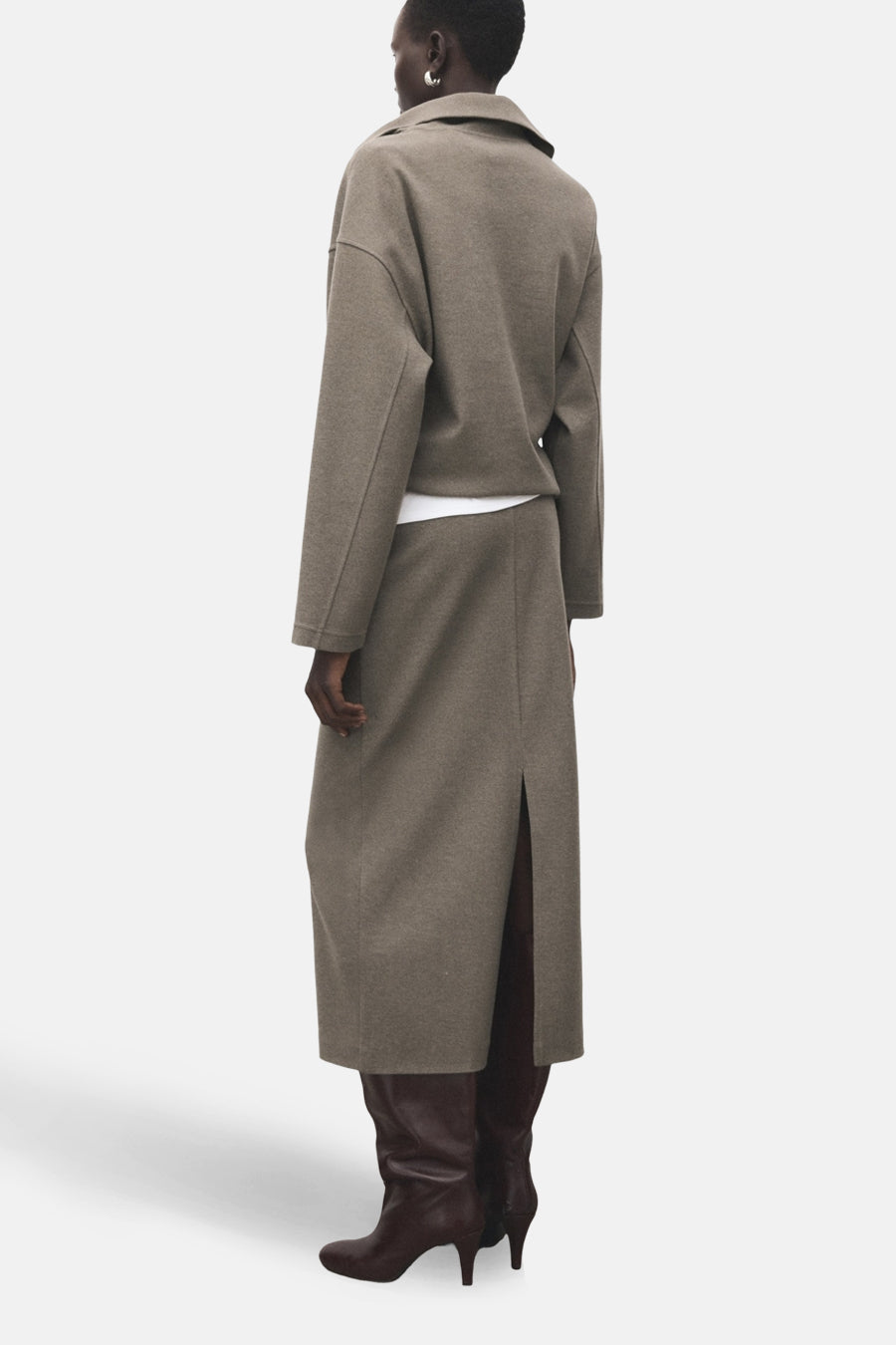 Jupe longue marron de MANGO, fendue à l'arrière, portée avec un haut court blanc et des bottes en cuir marron.
