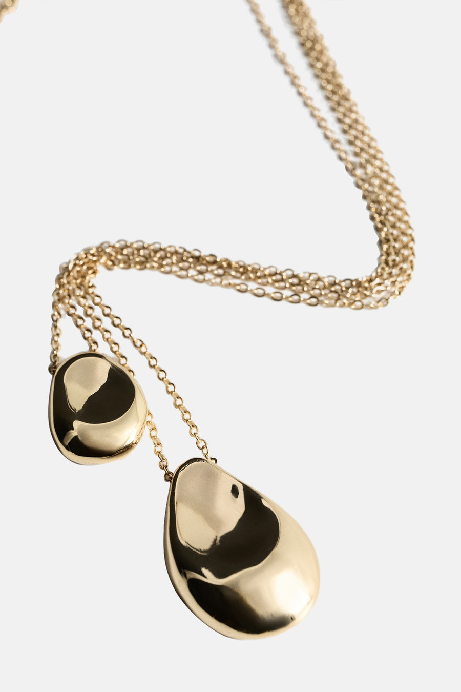 Collier court doré de MANGO, avec deux breloques aux formes organiques et réfléchissantes.