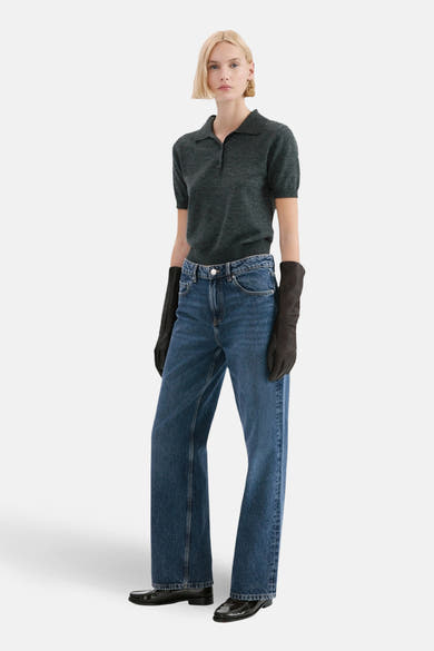 Rechte donkerblauwe spijkerbroek van MANGO, gedragen met een grijze polo en zwarte handschoenen.