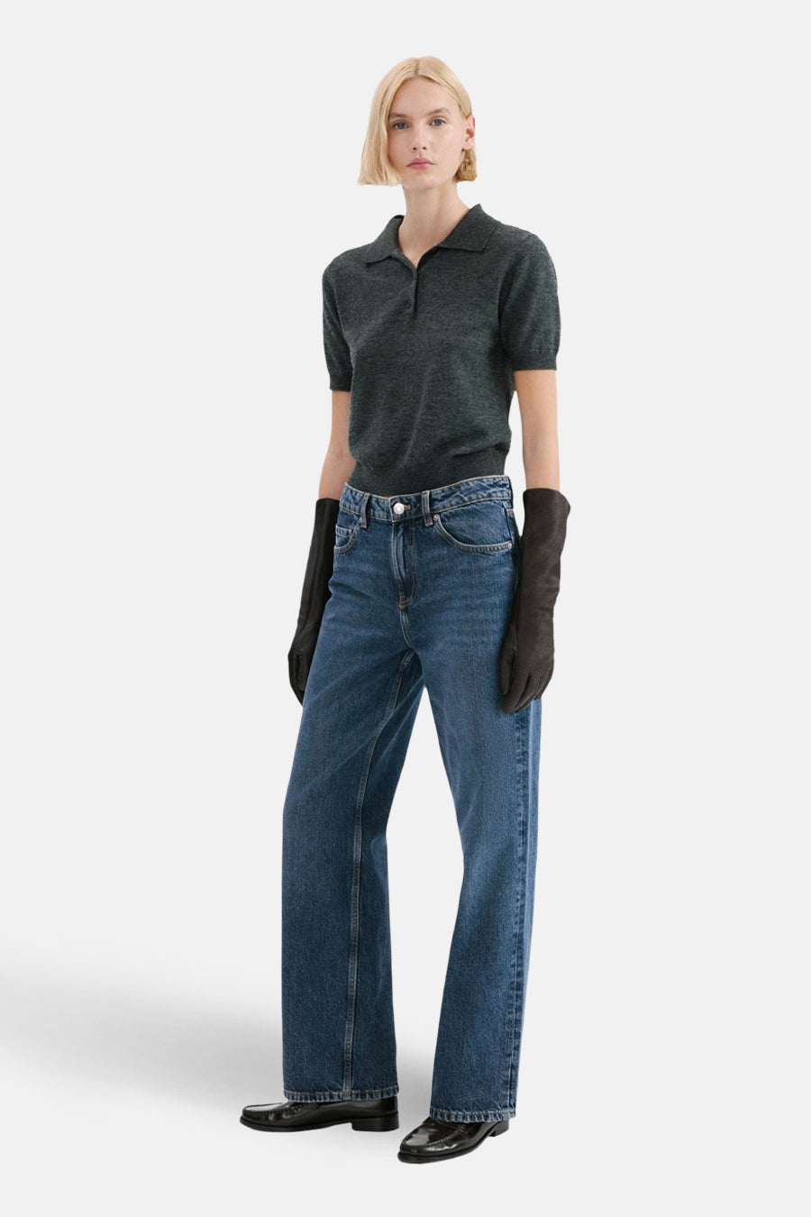 Rechte donkerblauwe spijkerbroek van MANGO, gedragen met een grijze polo en zwarte handschoenen.