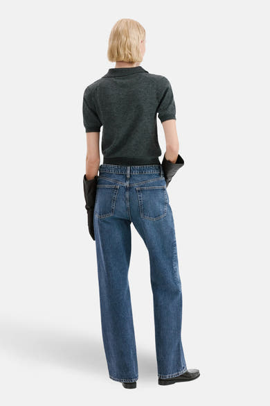Jean droit en denim bleu foncé de MANGO, porté avec un polo gris et des gants noirs.