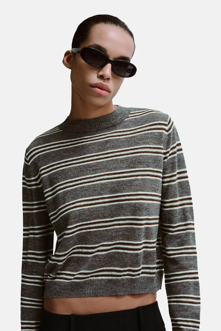 Pull à col rond gris MANGO à rayures blanches et marron, porté avec des lunettes de soleil noires.