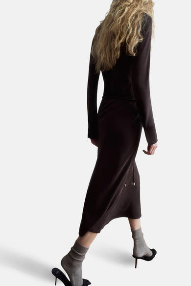 Robe à manches longues brune de MANGO, vue de dos, portée avec des chaussettes grises et des chaussures noires.