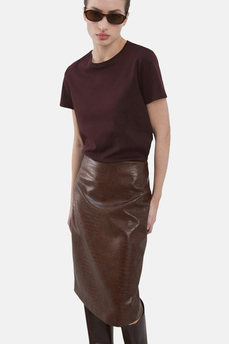 T-shirt bordeaux à manches courtes de MANGO, porté avec une jupe en cuir marron à motif crocodile.