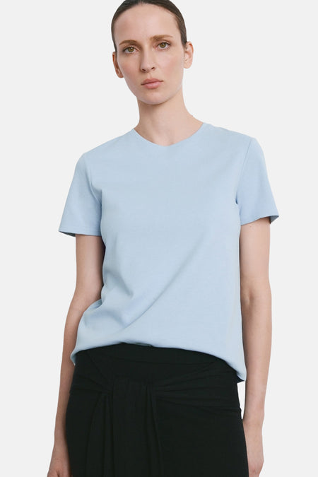 T-shirt bleu à manches courtes de MANGO, porté avec une jupe noire à taille nouée.