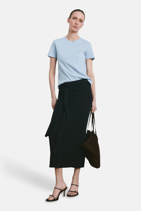 T-shirt bleu de MANGO, porté avec une jupe noire nouée et des talons à lanières.
