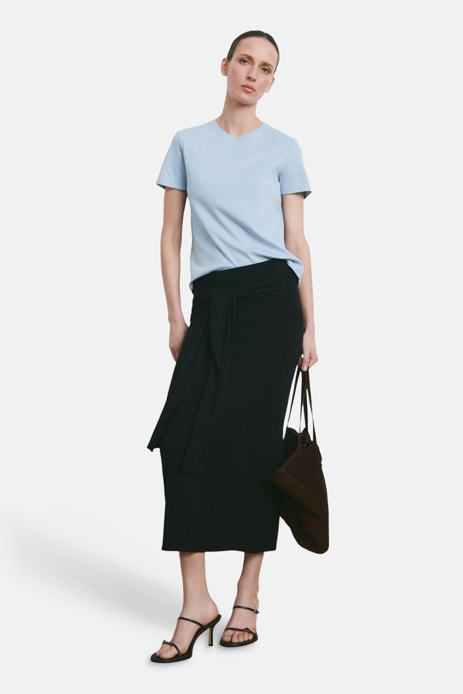 Blauw T-shirt van MANGO, gedragen met een zwarte wikkelrok en sandalen met bandjes.