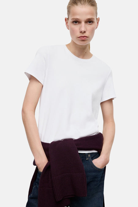 T-shirt blanc à manches courtes de MANGO, porté avec un pull noué à la taille et un jean.