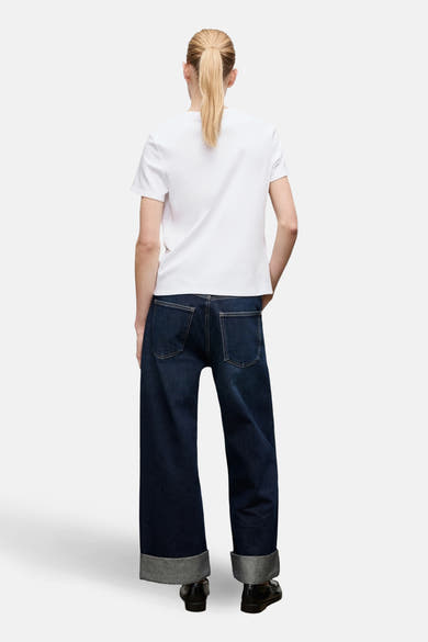 T-shirt blanc à manches courtes de MANGO, vue de dos, porté avec un jean bleu ample à revers.