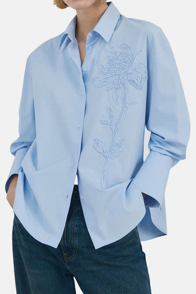 Blauwe blouse met lange mouwen van MANGO, met plooien aan de achterkant, gedragen met een wijde spijkerbroek en bruine schoenen.