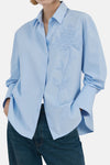 Blauwe blouse met lange mouwen van MANGO, met plooien aan de achterkant, gedragen met een wijde spijkerbroek en bruine schoenen.