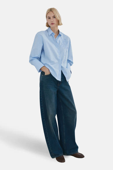 Blauwe blouse met lange mouwen van MANGO, versierd met bloemenborduursels aan de voorkant, gedragen met een wijde jeans.