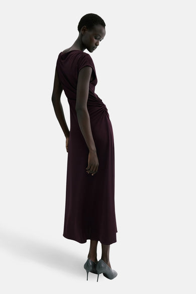 Robe bordeaux de MANGO, avec détail froncé latéral, portée par une mannequin avec des escarpins gris à talons aiguilles.