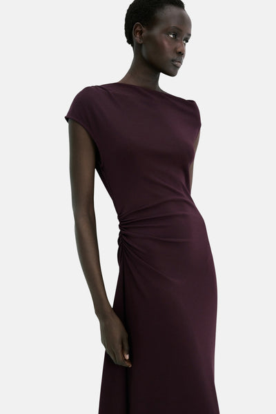 Robe bordeaux de MANGO, avec une encolure bateau et un drapé asymétrique sur le côté.
