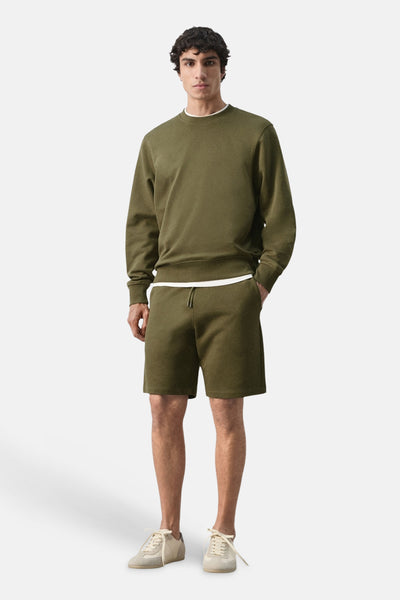 Sweat-shirt kaki col rond de MANGO, porté avec un short et des baskets beiges.
