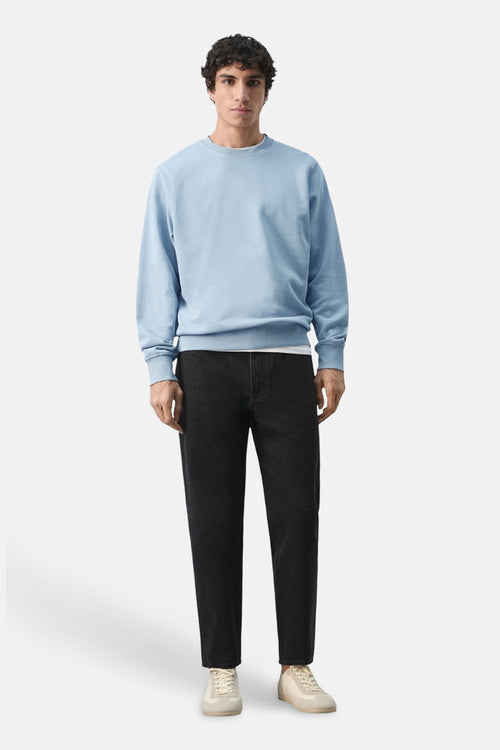Sweat bleu de MANGO, porté avec un jean noir et des baskets beiges.