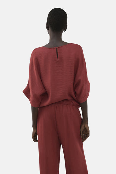 Blouse à manches courtes marron de MANGO, avec manches amples et détail goutte au dos, portée avec un pantalon assorti.