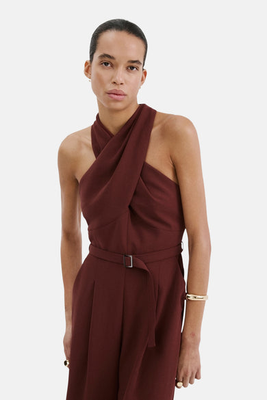 Combinaison brune par MANGO, avec un col drapé croisé, une ceinture et un bracelet doré.
