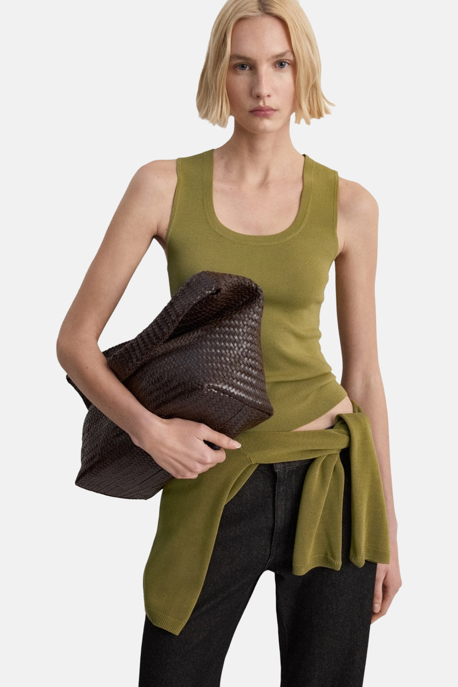 Débardeur kaki MANGO porté avec un pantalon noir et un pull vert noué à la taille.