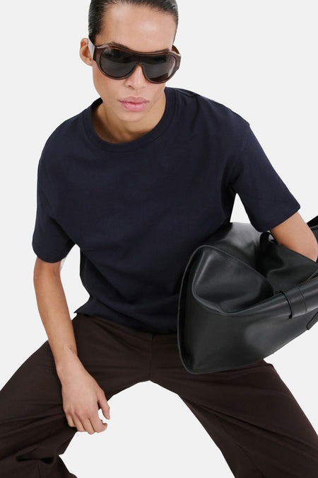T-shirt bleu marine de MANGO, porté avec un pantalon marron et de lunettes de soleil.