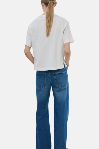 T-shirt blanc de MANGO, manches courtes, porté avec un pantalon en denim bleu large, vue de dos.