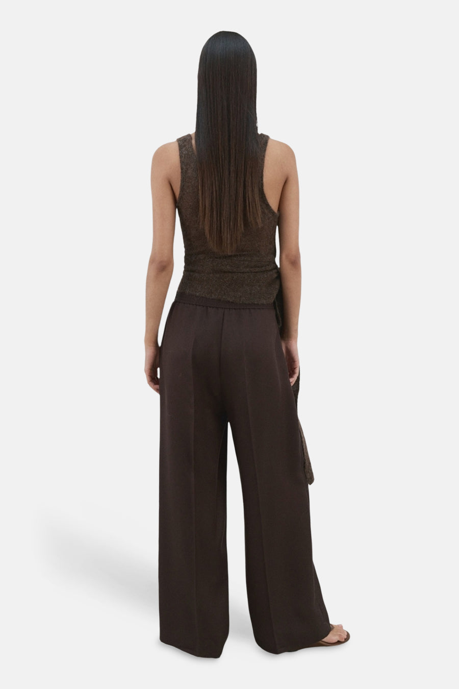 Pantalon large brun de MANGO, avec une taille élastique et une jambe ample tombant sur des sandales.