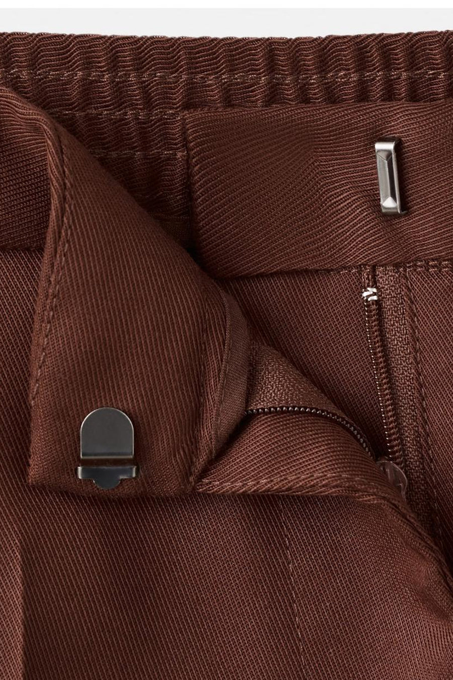 Pantalon marron de MANGO, détail de la fermeture à crochet métallique et de la braguette zippée.
